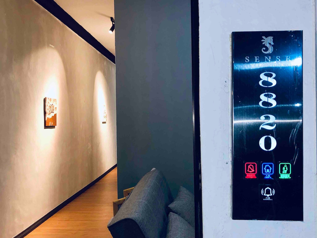 A modern corridor showcases a sleek elevator panel marked with the number 8820. Dim lighting highlights artwork on the walls, while a comfortable sofa is positioned nearby, inviting guests to relax as they await their journey.