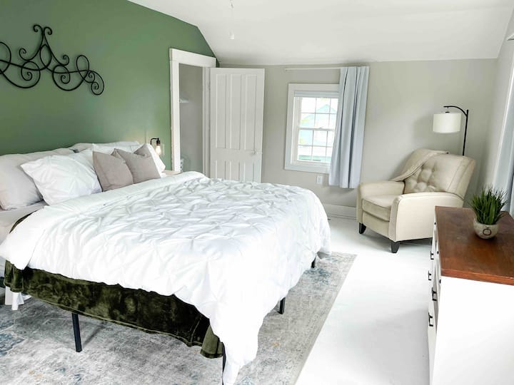 Velika bračna soba s mnogo prirodnog svjetla, prostorom za sjedenje, komodom i ogledalom pune dužine. 