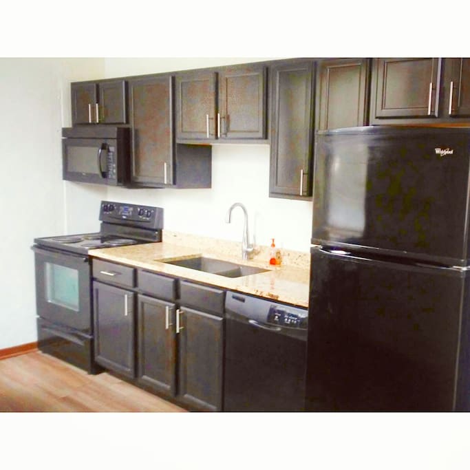 Large kitchen, with some essentials. A pan with utensils, cups, wine glasses, double compartment sink, dishwasher, refrigerator with ice maker.