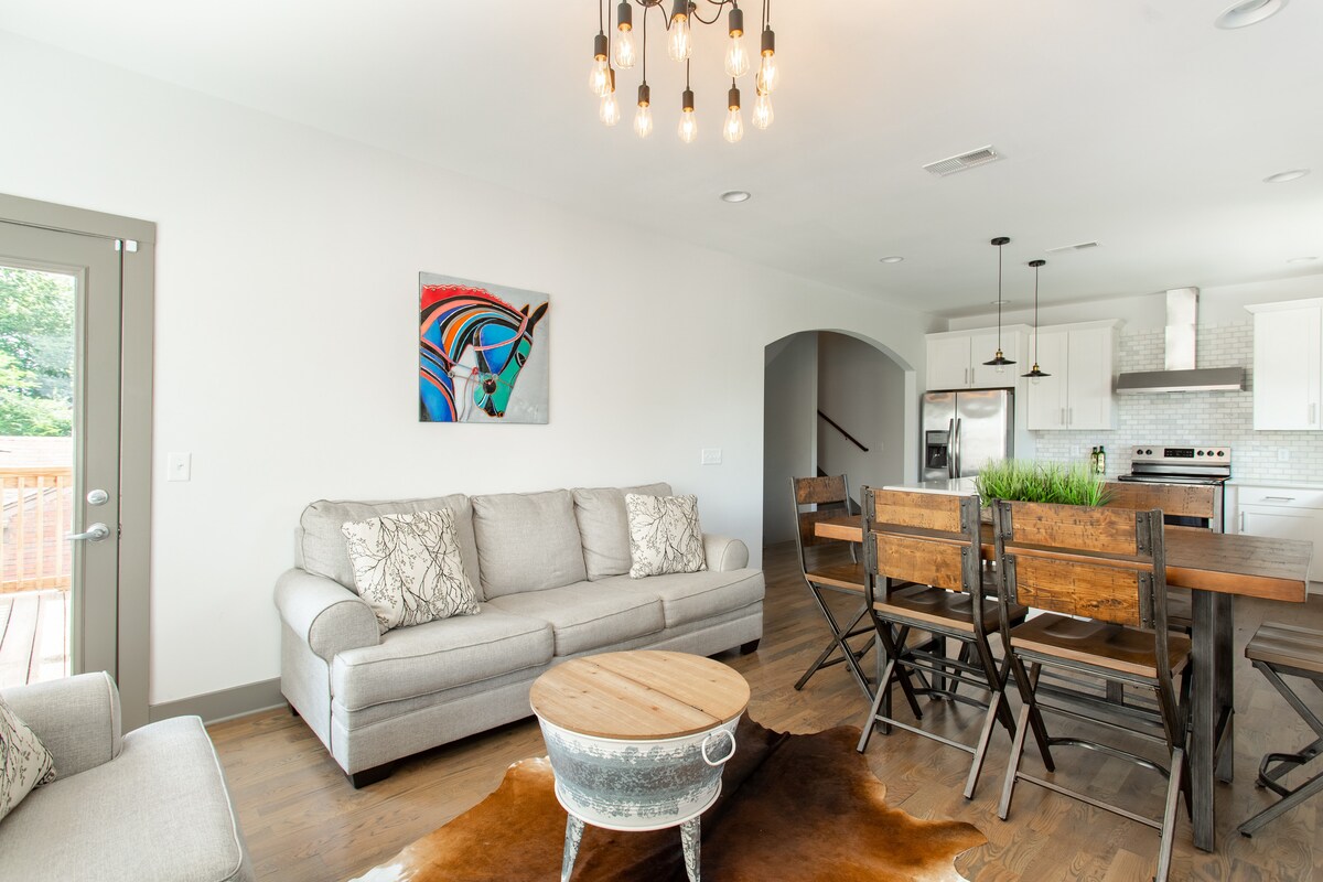 开放式厨房/客厅，配备餐椅、厨房岛台的吧椅、咖啡桌、拉伸式沙发和许多窗户，可享受阳光和/或在百叶窗下保持隐私。 有很多灯光。