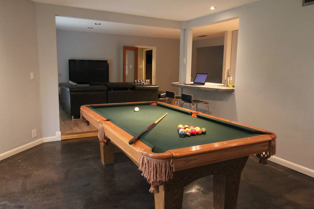 Custom pool table over looking the large screen television and laptop workspace/bar top.