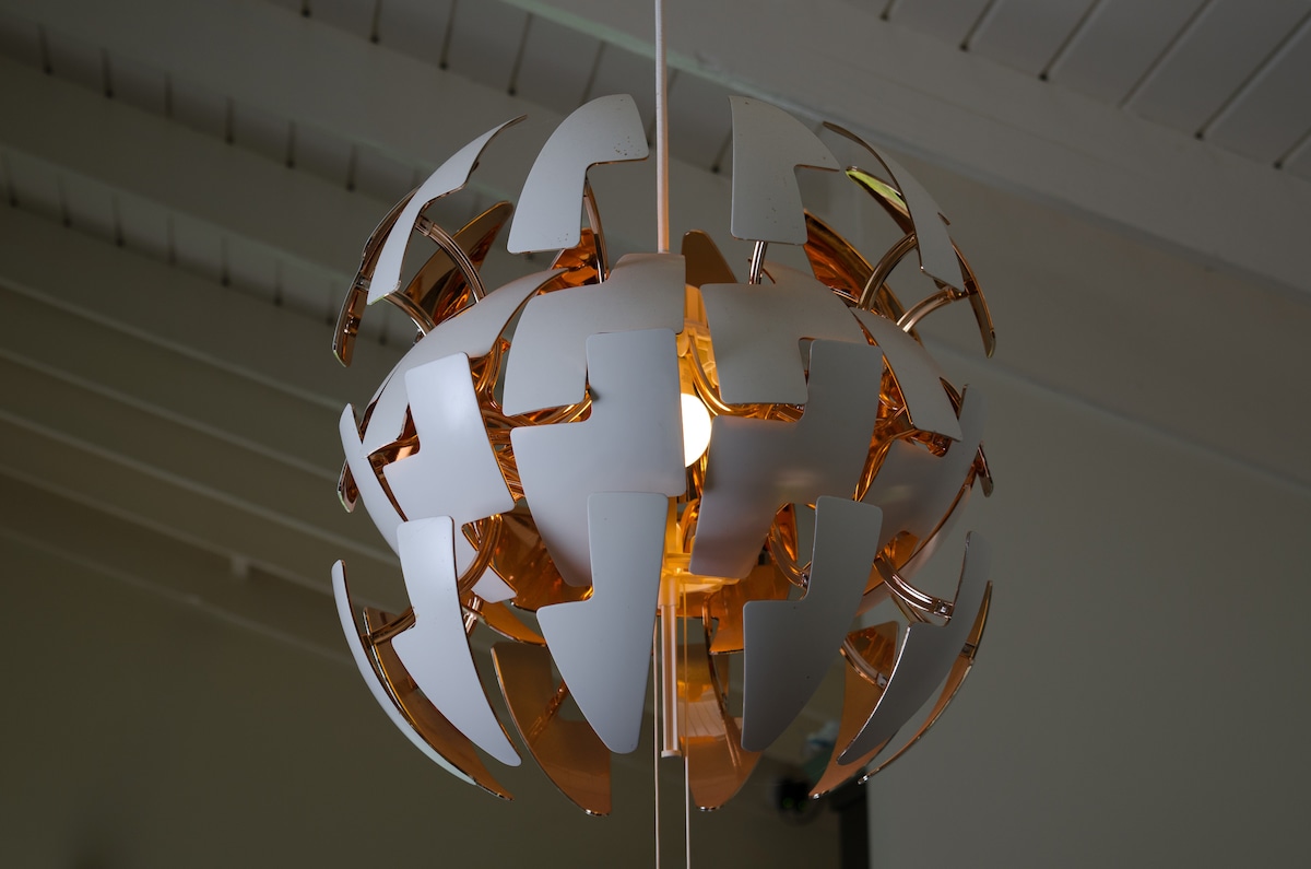 A modern pendant light features a distinctive geometric design with white and metallic elements. The light source is centrally located, surrounded by the sculptural fixture, creating a unique focal point in the room.