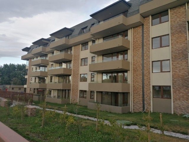 A modern three-story building is presented, featuring an attractive facade with stone accents and multiple balconies. The landscaping includes pathways and grass, providing a pleasant outdoor environment. Ample windows allow for natural light, contributing to the overall inviting appearance of the property.