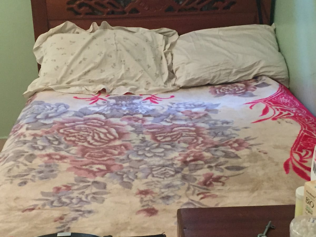 A spacious bed is adorned with a soft floral blanket. Two pillows rest at the head of the bed, and light colors are featured throughout. A bedside table is visible, offering a subtle contrast to the bedding.