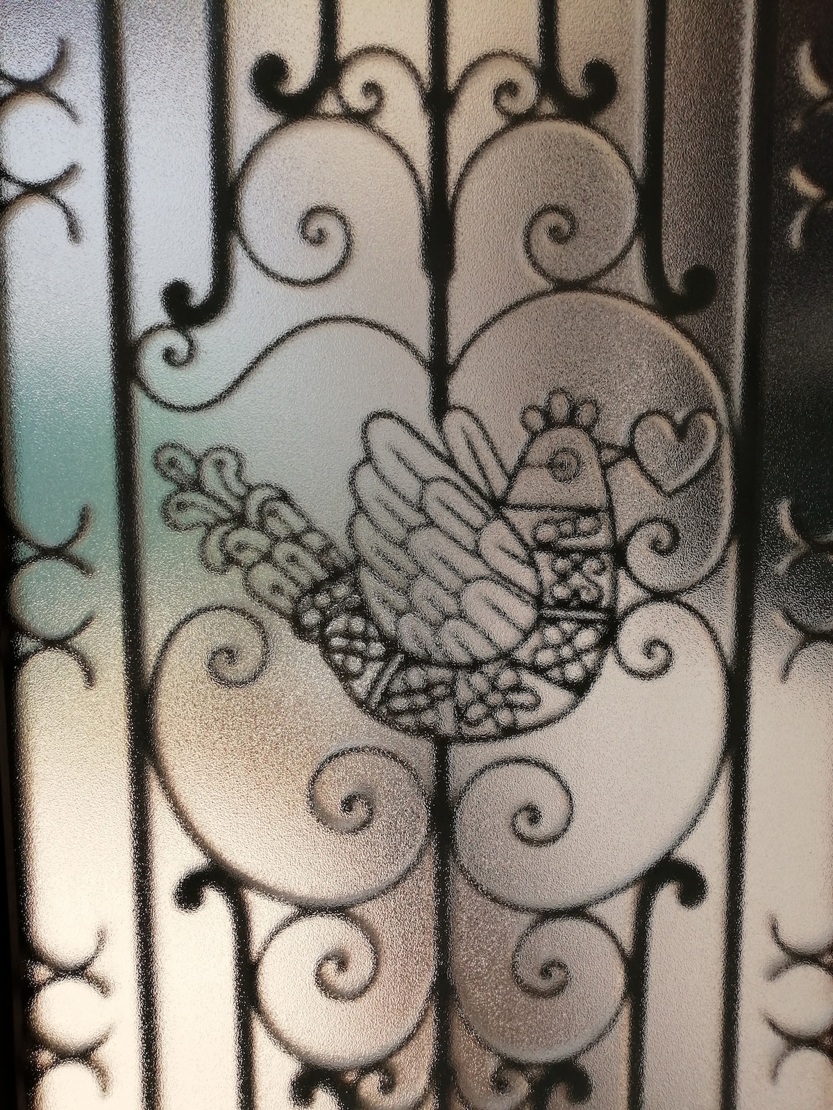 A decorative frosted glass door features an intricate design of a bird, surrounded by ornate patterns. The image highlights the craftsmanship with smooth curves and textured detailing, creating a charming focal point. Soft light filters through, enhancing the overall visual appeal.