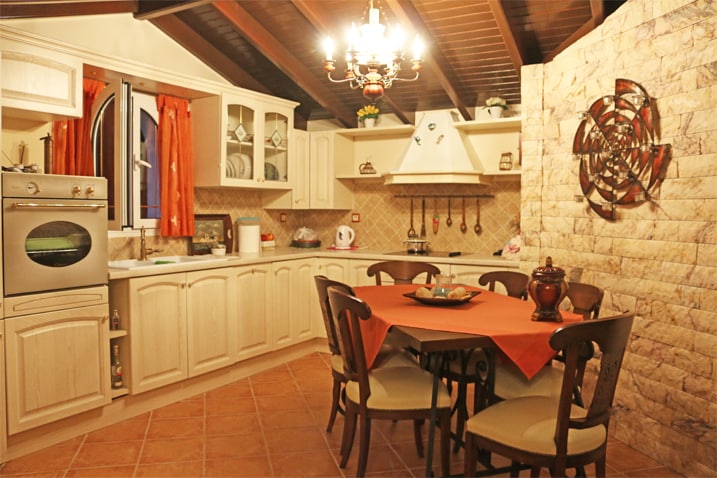 A well-appointed kitchen features a table set for six, surrounded by wooden chairs. A stove, oven, and ample cabinetry create a functional cooking area. Decorative elements include warm orange curtains and a metallic wall art piece, enhancing the inviting atmosphere of the space.