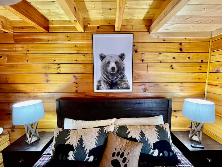 "Bear Den" ina kitanda aina ya king, samani za chumba cha kulala cha kahawia, runinga kubwa janja, beseni la jacuzzi na bafu lililounganishwa.