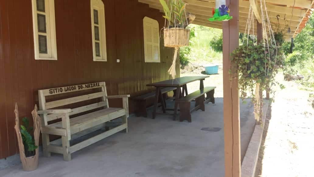 A shaded outdoor seating area is furnished with a wooden bench and a long table, surrounded by natural greenery. The space features a covered porch that leads to a tranquil view of the surrounding landscape.