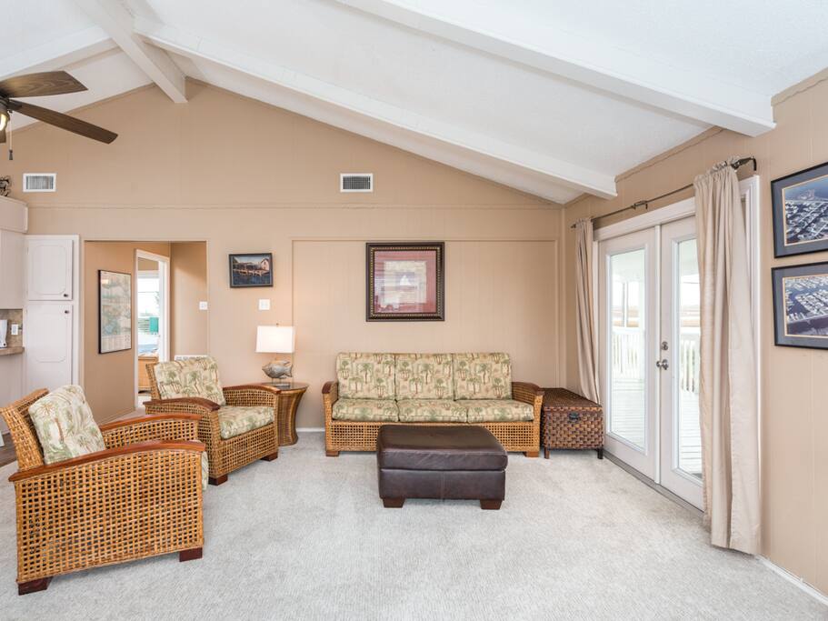 The living area features modern wicker furniture with tropical print cushions and a 40” flat-screen TV