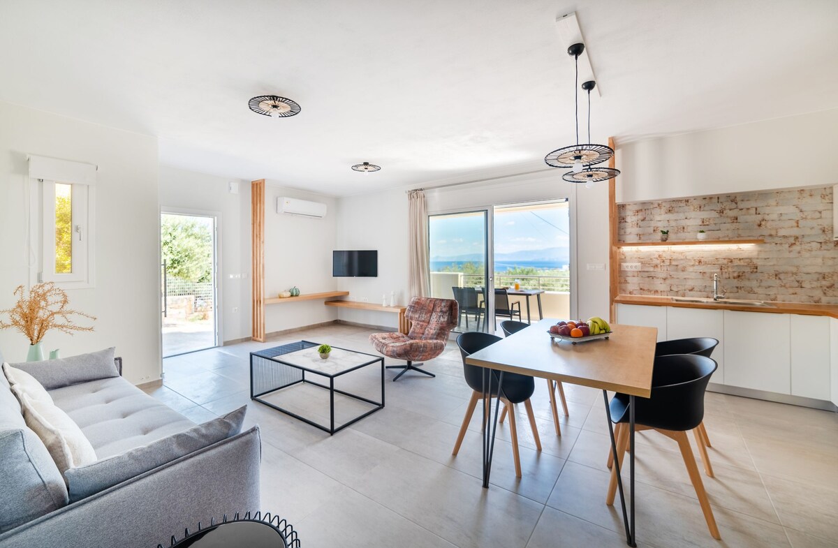 A modern living room is featured, showcasing a comfortable sofa and a stylish armchair. A coffee table centers the space, while a dining table with black chairs is visible nearby. Large glass doors open to a view of the outdoors, enhancing natural light.