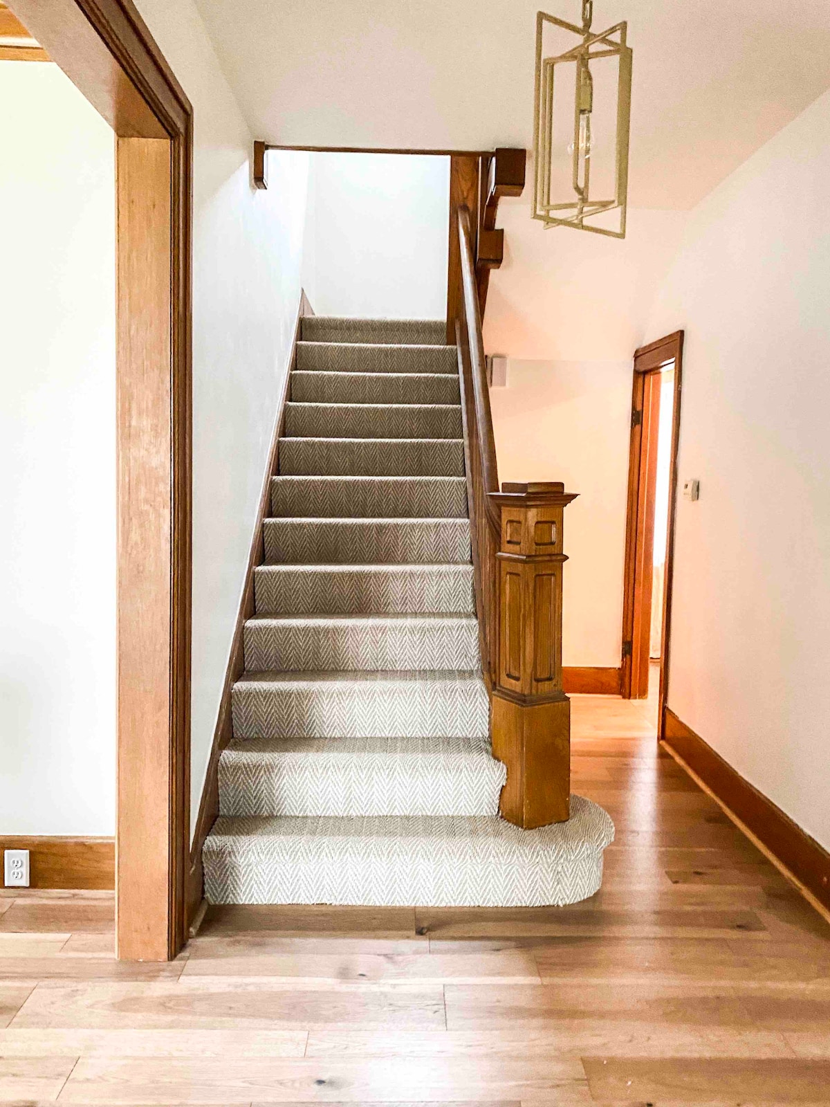 A well-lit staircase is lined with soft carpet, leading upwards to the second floor. Rich wooden banisters and trims provide a classic touch, while natural light illuminates the entryway. The clean lines and neutral colors contribute to an open and inviting atmosphere.