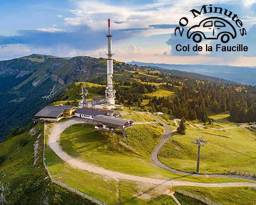 A panoramic view of Col de la Faucille presents lush green mountains and a walking path leading to a modern building with antennas. The area is surrounded by dense trees and open fields, showcasing a part of the scenic Jura landscape under a partially cloudy sky.