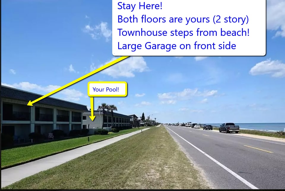 A beachside townhouse is shown, featuring two stories with palm trees and a clear view of the ocean in the background. A spacious garage is visible on the front side. The image captures a wide road lined with greenery, inviting trails for walking.