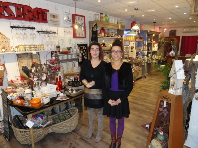 An inviting shop interior features a variety of decorative items and gifts displayed on wooden shelves and tables. The warm lighting enhances the colorful merchandise, including pottery, textiles, and seasonal decorations. A cozy atmosphere is created with wooden flooring and an assortment of decorative elements.