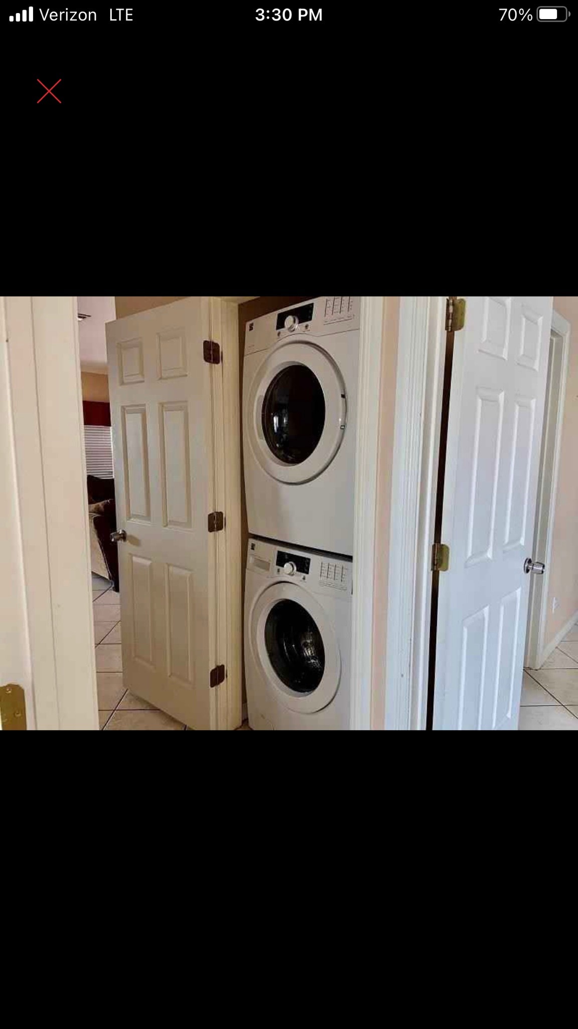 A stacked washer and dryer are situated behind closed doors in a designated laundry area. The neutral-colored doors complement the surrounding light-colored walls and tiled flooring, creating a tidy and functional space.