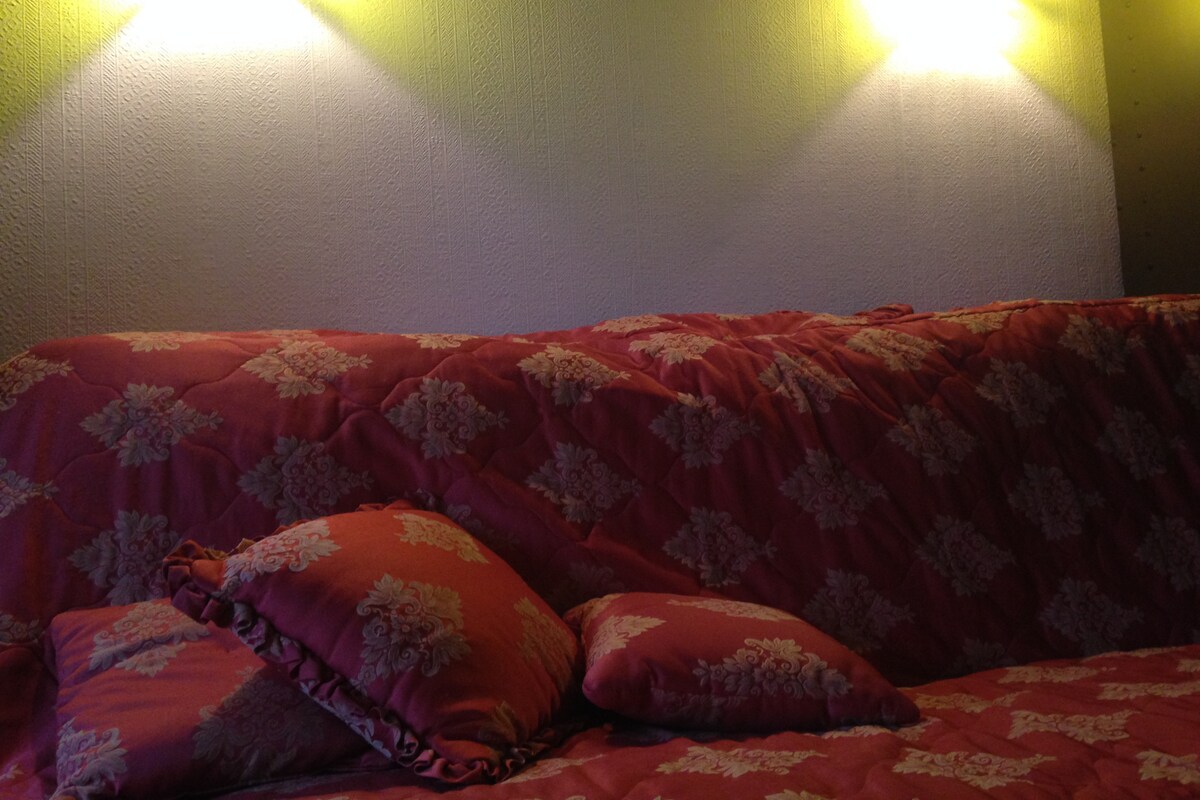 A sofa adorned with a rich, patterned cover features several decorative cushions. Soft lighting from two wall sconces creates a warm glow, enhancing the cozy feel of the seating area.