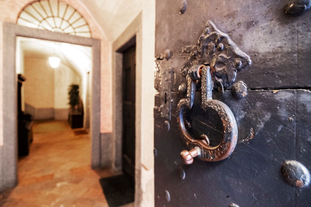 An ornate metal door handle is prominently featured in the foreground, showcasing intricate designs. A soft-lit entrance leads into a corridor, where the warm tones of the walls and flooring create a welcoming ambiance.