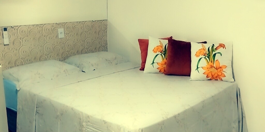 A well-appointed sleeping area features a spacious bed layered with an elegant patterned blanket. Colorful decorative pillows with floral designs add a touch of vibrancy, while light walls create a bright, inviting atmosphere.
