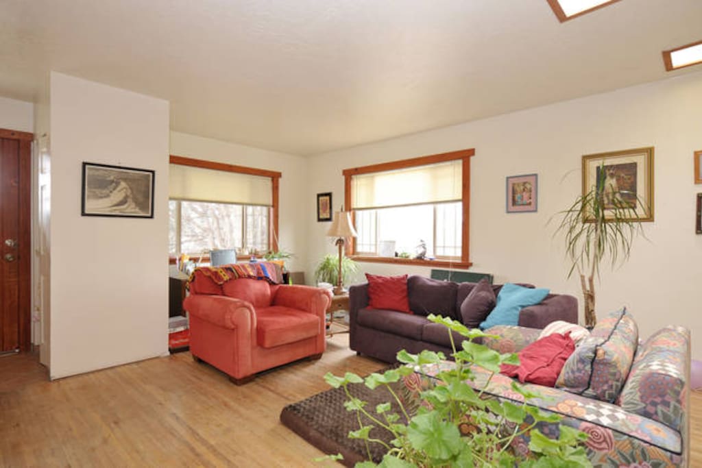 Open concept livingroom with hardwood floors, skylight and two large windows.