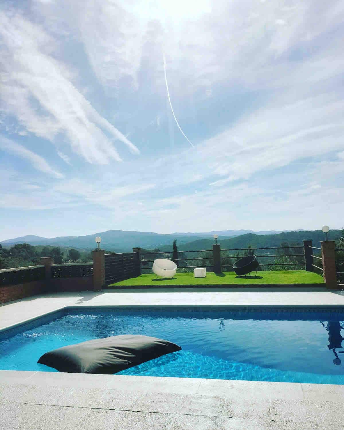 A serene outdoor space showcases a private pool under a bright sky. Lush green grass surrounds the pool area, accented by modern lounge furniture. Scenic mountain views stretch in the background, enhancing the tranquil atmosphere of this relaxing retreat.
