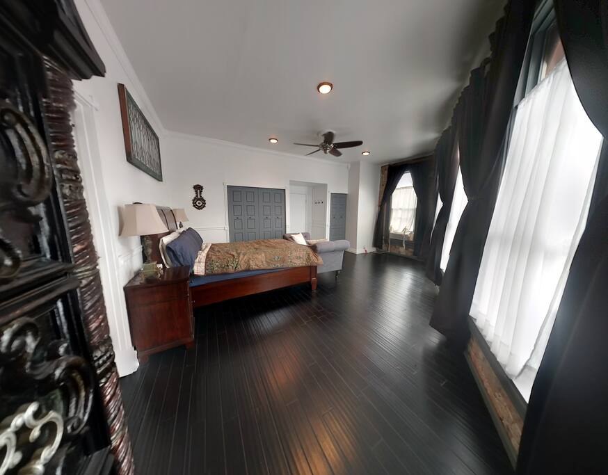Large Bedroom (350 sq. ft.) with a queen sized bed, settee, four tall windows, heating/air conditioning, ceiling fan, and closet space.