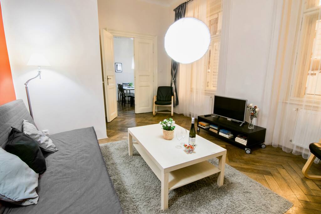 A spacious living room with an original parquet floor. Equipped with folding sofa, two armchairs and television