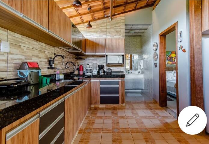 The kitchen features wooden cabinetry and granite countertops, illuminated by natural light from a nearby window. A variety of appliances, including a microwave and coffee maker, are neatly arranged. The tiled floor adds a cohesive look, complementing the warm tones of the wooden decor.