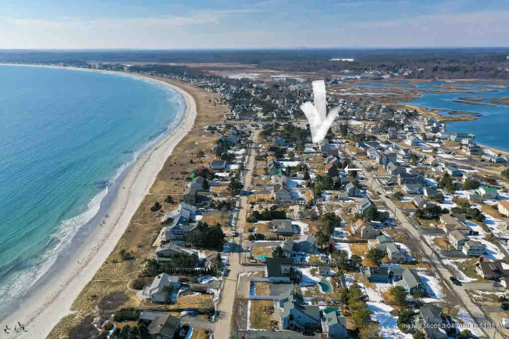 An overhead view showcases a coastline lined with sandy beaches. The image highlights a peaceful neighborhood filled with homes, surrounded by natural landscapes and waterways, with easy access to both the beach and marsh.