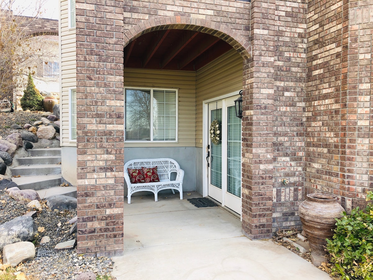 A covered entryway features a white bench adorned with decorative pillows. Stone steps lead to a landscaped area with boulders, while a large clay pot is positioned nearby. A glass door with an elegant design offers access to the interior.