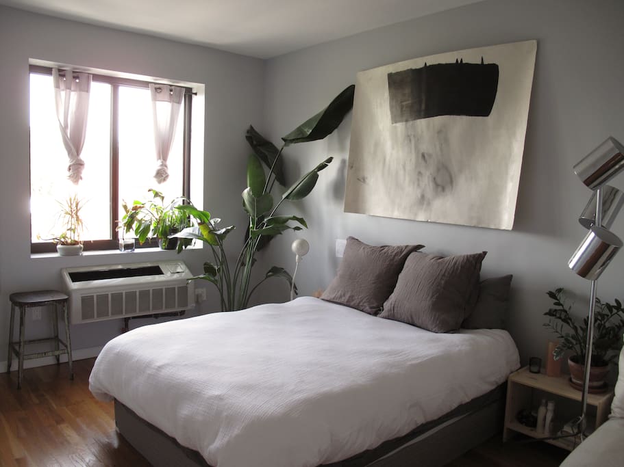 Bedroom with queen size bed, corner lounge chair, a closet, and plants + light