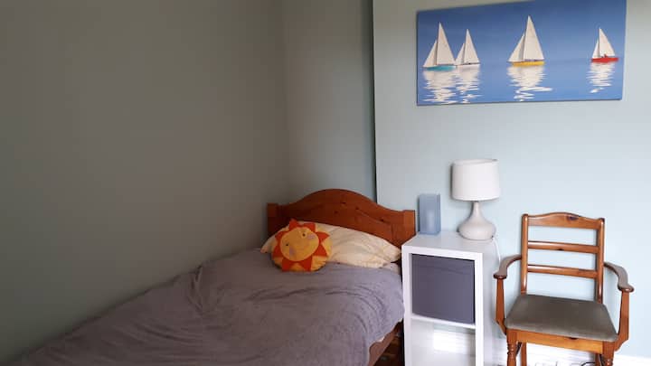 Cuarto dormitorio (en la planta baja) con cama individual, puertas de patio al jardín trasero y escritorio de oficina.  