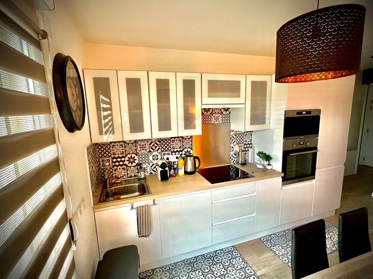 A modern kitchen is featured, equipped with a built-in stove, oven, and a sleek countertop. The cabinetry is white with glass fronts, and patterned tiles add a stylish touch to the backsplash. A pendant lamp provides ambient lighting, enhancing the workspace.