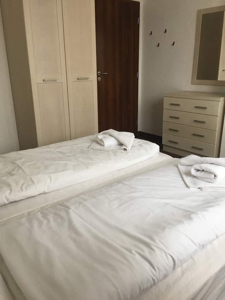 Spavaća soba u prizemlju koja se sastoji od dva kreveta za jednu osobu, ormara i komode s crtežima. Iznad škrinje nacrta ogledalo. 