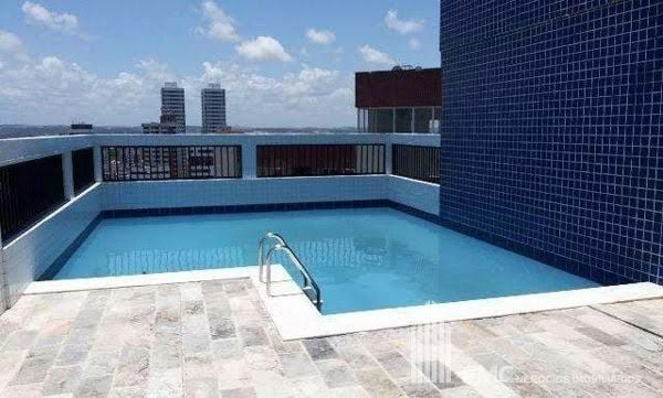 A spacious rooftop pool is featured, surrounded by a tiled deck and railing. Sunlight reflects off the clear water, creating a relaxing atmosphere. The skyline is visible in the background, enhancing the setting.