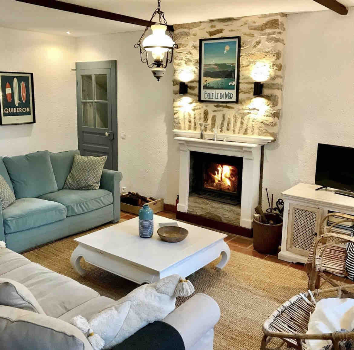 A cozy living room features an attractive stone fireplace, complemented by two comfortable sofas and a coffee table. Soft lighting from wall sconces creates a warm atmosphere. A flat-screen TV is positioned to one side, with natural fibers underfoot enhancing the inviting space.