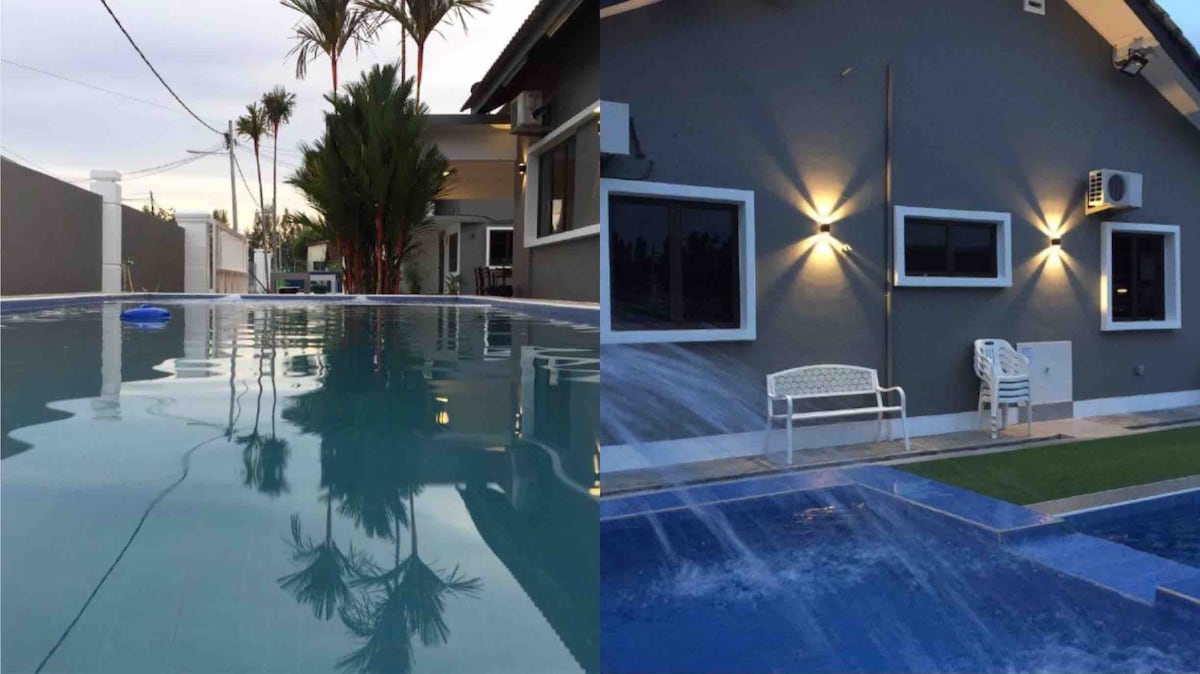 Two inviting swimming pools are showcased, featuring clear blue water reflecting surrounding palm trees. A pathway leads to the pools from two adjacent villa structures, where outdoor seating is available. Ample natural light enhances the calm ambiance, highlighted by soft wall lighting.