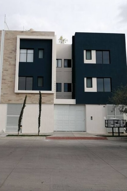 The modern building features a two-tone facade, with dark blue and light gray sections. Large windows are visible on the upper floors, allowing for ample natural light. A garage door is located on the ground level, with minimal landscaping and clear views of the surrounding area.