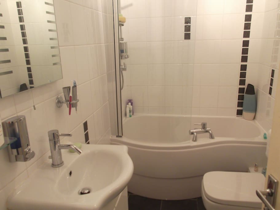 Small bathroom with curved bath & overhead shower. Heated towel rail