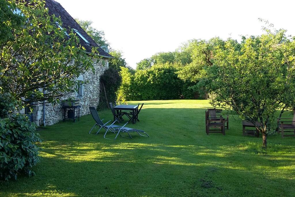 jardin avec tables, chaises, transats et barbecue type plancha.