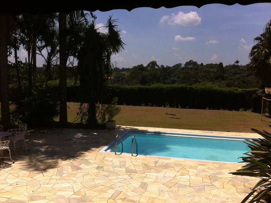 Piscina, com cadeiras e guarda sol e campo de futebol