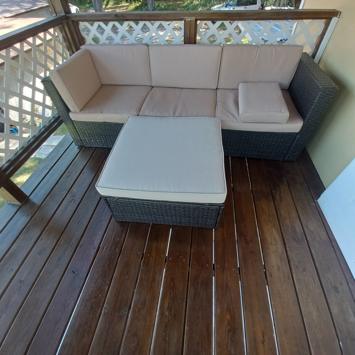 A cozy balcony area features a comfortable sectional sofa with soft beige cushions and a matching ottoman. The wooden deck appears polished, enhancing the inviting atmosphere, ideal for relaxation or enjoying scenic views.