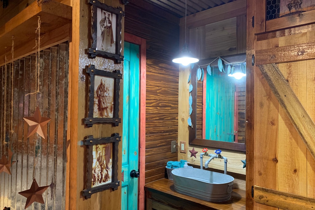 A rustic bathroom features wooden walls and vibrant turquoise accents. A spacious wooden countertop holds a unique basin sink, complemented by star-themed decor. Vintage-style lighting illuminates the area, enhancing the welcoming and functional layout.