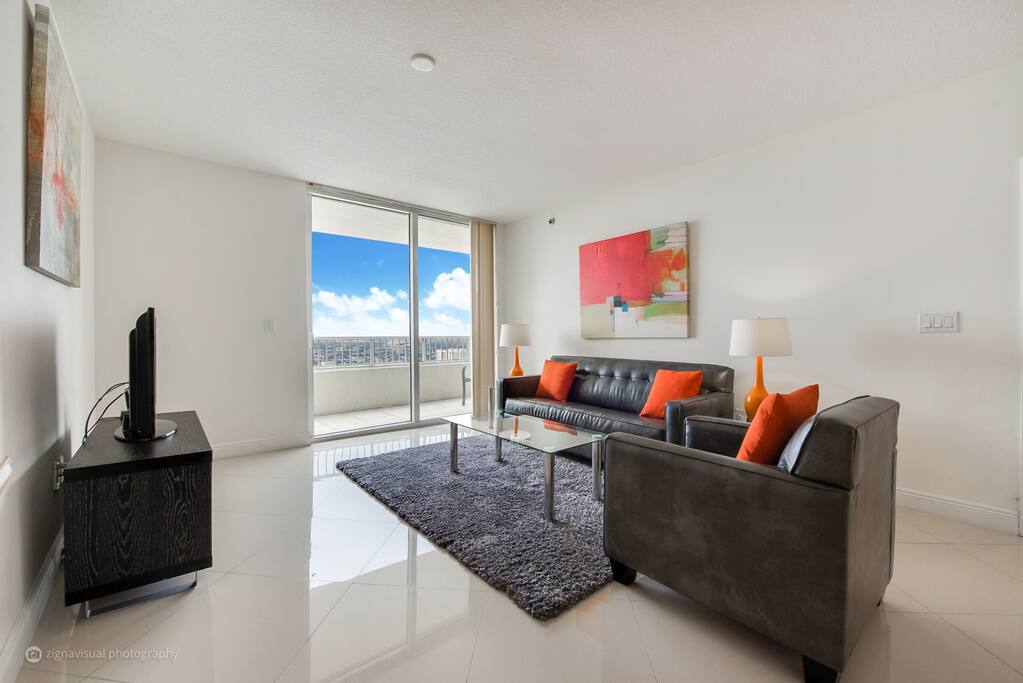 Living room with sofabed, club chair and floor to ceiling doors that lead to private balcony