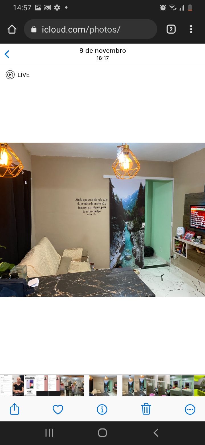 A living area is featured with light-colored furniture and a marble-patterned table. A printed wall decoration depicts a serene forest scene. Two pendant lights provide ambient lighting, while a television is positioned on a low cabinet, enhancing the room's functionality.