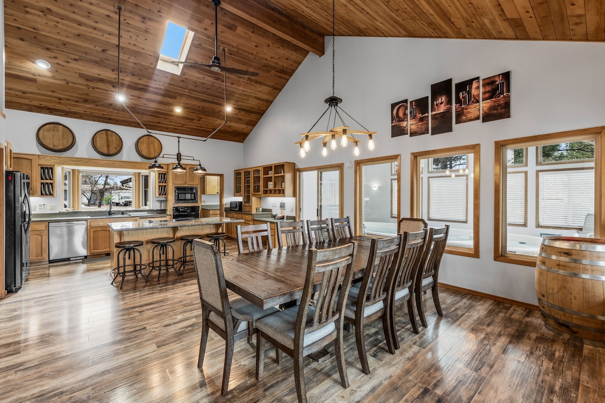 The open kitchen and dining area features high wooden ceilings and large windows, allowing ample natural light. A spacious wooden dining table with multiple chairs accommodates larger groups. A well-equipped kitchen with modern appliances and wooden cabinetry is visible, enhancing the inviting atmosphere.