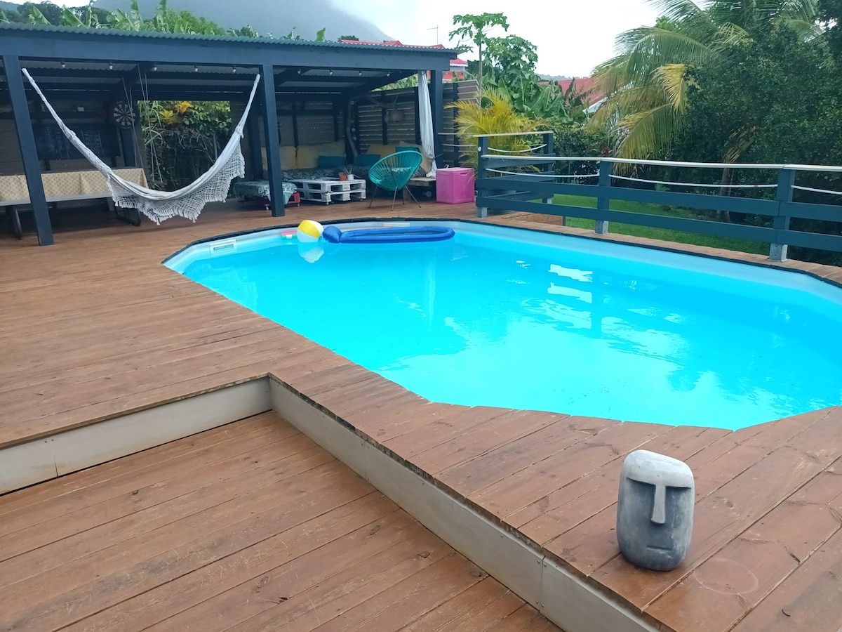 A private wooden deck surrounds a turquoise swimming pool, with a lounge chair and a vibrant beach ball resting nearby. Lush greenery is visible in the background, adding to the serene outdoor space.