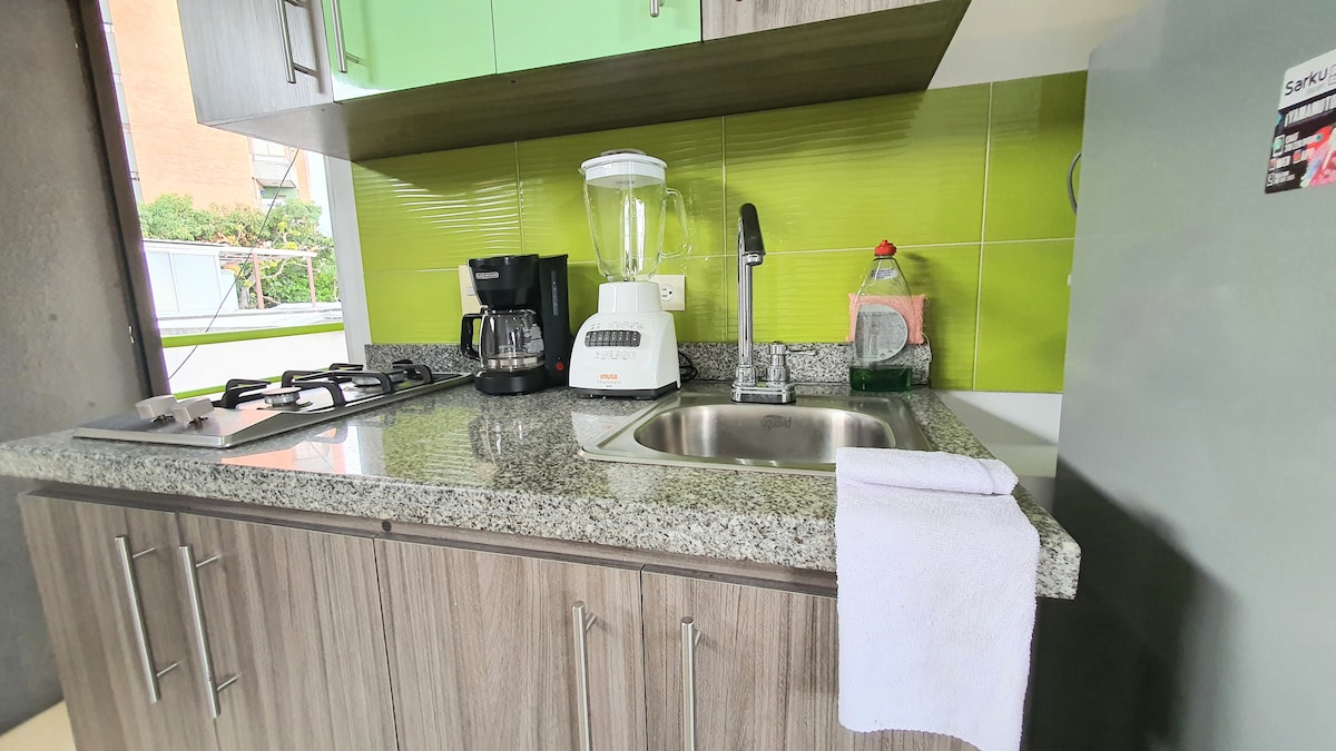 A modern kitchen area is shown, featuring granite countertops and a sleek design. Appliances include a coffee maker, blender, and stove. The backsplash is accented with vibrant green tiles, enhancing the inviting atmosphere of the space.