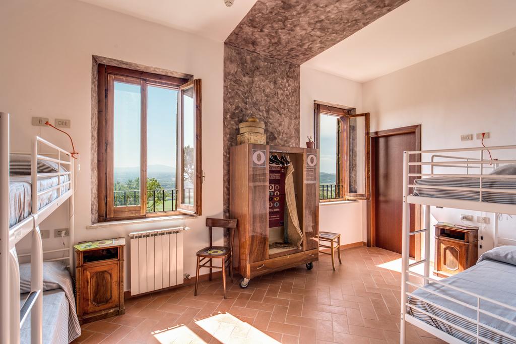 A spacious dormitory room features two sets of bunk beds along with a wooden wardrobe. Two windows offer a view of the surrounding landscape, allowing natural light to illuminate the room. A chair is positioned near the window, enhancing the inviting atmosphere.