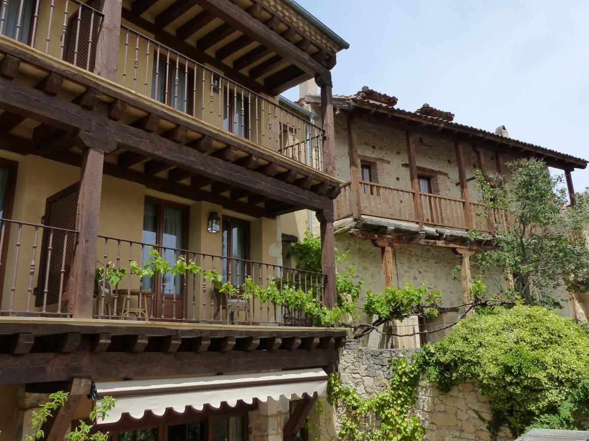A charming building exterior features multiple balconies with wooden railings, surrounded by lush greenery. The arrangement showcases a blend of rustic stone and traditional wooden architecture. Sunlight filters gently through the leaves, highlighting the inviting atmosphere of this inviting space.