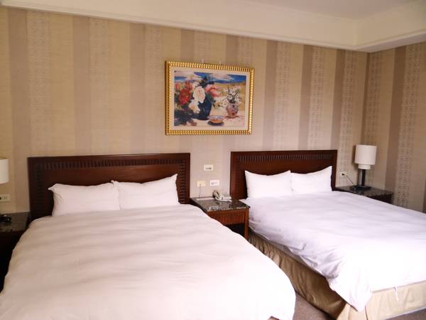 An inviting sleeping area features two spacious beds dressed in white linens. A painting decorates the wall above the beds, while two bedside tables with lamps are positioned on either side. Soft striped wallpaper provides a warm backdrop to the room.